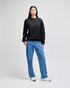 A black crewneck sweatshirt worn by a model, paired with blue jeans and casual shoes. The product has a logo.