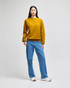 A model wearing a mustard yellow crewneck sweatshirt paired with light blue jeans and white shoes, featuring a logo.