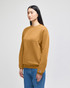 A mustard yellow crewneck sweatshirt worn by a model, featuring long sleeves and a logo on the sleeve.