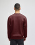 A crewneck sweatshirt in burgundy, featuring a back view and long sleeves, with a logo on the garment.