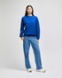 A woman wearing a bright blue crewneck sweatshirt paired with light blue jeans and white sneakers.