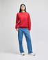 A red crewneck sweatshirt worn by a model with straight black hair, paired with blue jeans and white shoes.