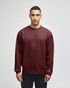 A maroon adult sweatshirt with a ribbed crew neckline and a logo on the sleeve, displayed on a model.
