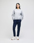 A grey women's crewneck sweatshirt paired with navy sweatpants and white sneakers, featuring a logo.
