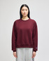 A maroon women's crewneck sweatshirt with a relaxed fit and a logo on the sleeve, paired with grey sweatpants.