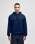 A navy blue pullover hooded sweatshirt with a front pocket and a logo. The model is wearing it against a plain background.
