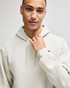 A light grey pullover hooded sweatshirt featuring a logo on the sleeve. Model wears it with a confident expression.