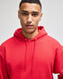 A red hooded sweatshirt with a front pocket and drawstring, worn by a young man. The sweatshirt has a logo.