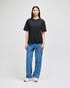A black Champion Adult Heritage Jersey T-shirt displayed on a model wearing blue jeans and white sneakers.