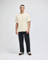 A beige Champion Adult Heritage Jersey T-Shirt worn by a model, paired with black trousers and casual shoes.