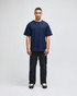 A navy t-shirt with short sleeves on a male model, paired with black pants. The shirt features a logo.