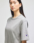 A grey Champion Adult Heritage Jersey T-Shirt is displayed on a model, featuring a logo on one sleeve.