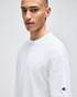 A white Champion adult heritage jersey t-shirt displayed on a model, featuring a logo on the sleeve.