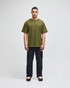 A green Champion Adult Heritage Jersey T-Shirt worn by a model, paired with black pants. The shirt features a logo.