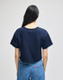 A navy cropped short sleeve t-shirt with a simple design and a logo on the back, worn with blue jeans.