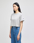 A grey cropped short sleeve t-shirt with a logo, styled on a model wearing blue jeans.