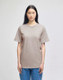 A light brown Champion adult short-sleeve t-shirt displayed on a model, paired with blue jeans. The shirt features a logo.