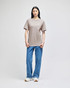 A light brown short-sleeve t-shirt displayed on a model, paired with blue jeans and white sneakers. The shirt has a logo.