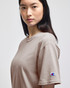 A beige Champion adult short-sleeve t-shirt featuring a logo on the left sleeve.