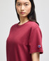 A maroon short-sleeve t-shirt featuring a logo on the sleeve.