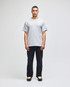 A grey short-sleeve t-shirt worn by a model, paired with dark pants. The shirt has a small logo on the sleeve.