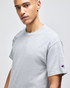 A grey short-sleeve t-shirt featuring a branded logo on the sleeve, displayed by a model.