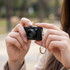 A compact black camera held in a person's hand, featuring a keychain attachment.