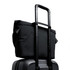 A black messenger bag positioned on top of a wheeled suitcase, featuring a retractable handle.