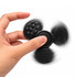 A black tactile fidget spinner is being spun between fingers, featuring different textured surfaces.