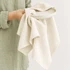 A medium cotton tea towel in a natural beige shade held over a ceramic plate, featuring a subtle texture.