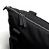 A black tote bag features a zip closure with leather zip pulls and a sturdy handle. It has a sleek, minimal design.