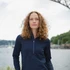 A woman stands by the water wearing a navy half-zip top. The image features a scenic background with a bridge.