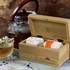 A bamboo tea box with compartments containing assorted tea bags, beside a glass of tea and a teapot.