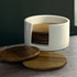 A white holder contains wooden coasters, with a few coasters resting on a dark surface.