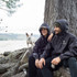 A black windbreaker worn by two people sitting by a tree, with a small dog nearby. The jackets have a logo on them.
