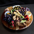 A wooden lazy Susan with an assortment of grapes, strawberries, cheese, crackers, olives, and dried meats.