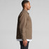 A man wears a brown heavy canvas jacket with a side view, featuring a pocket and a logo.