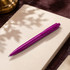 A purple plastic pen resting on an open notebook, with soft shadows in the background.