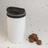 A reusable white coffee cup with a black lid, accompanied by several brown chocolate cups.