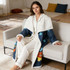 A blanket featuring a blue and white design with colourful patterns, displayed on a couch with a model wearing pyjamas.