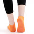 A pair of orange low cut kids gripper socks with textured soles, showcased from the back, worn with black leggings.