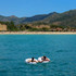 An inflatable swim ring in white floats on blue water, with a person lounging on it in a sunny outdoor setting.