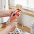 A pair of hands squeezing biodegradable dishwashing cloths under running water, featuring orange and beige colours.