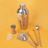 A drink bottle with a shiny stainless steel shaker, strainer, jigger, tongs, and stirring spoon, all in silver.