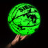 A glowing green PU basketball with splatter design, held in a hand against a dark background.