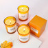 Three orange glass candles, each with a different label, grouped together on a light background with a yellow box.