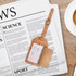 A cork luggage tag in natural tones, featuring a fold-out section for personal information, resting on a newspaper.
