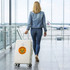 A woman walks through an airport with a white ribbed ABS suitcase featuring a logo. The suitcase is wheeled for easy transport.