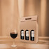 A drink bottle packaging featuring a kraft cardboard box for three wine bottles, with a glass of red wine beside it.