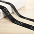 A black ribbed fabric ribbon with a logo, laid across a light surface next to a package.